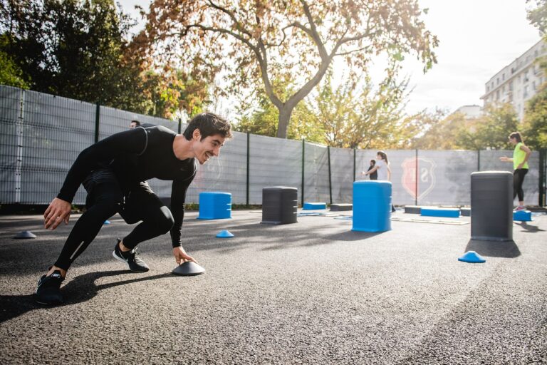 Man performing cardio exercises on the ground, and maintaining a focused expression. The background shows an outdoor fitness space with natural lighting, emphasizing movement and endurance.