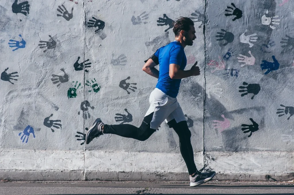 A man training for a 5k on the sidewalks, wearing black sneakers, a blue T-shirt, and white shorts for comfort.