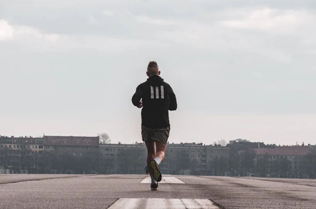 A man wearing a black and white striped hoodie pullover, shorts, shoes, and white socks for cardio training in the outside environment.