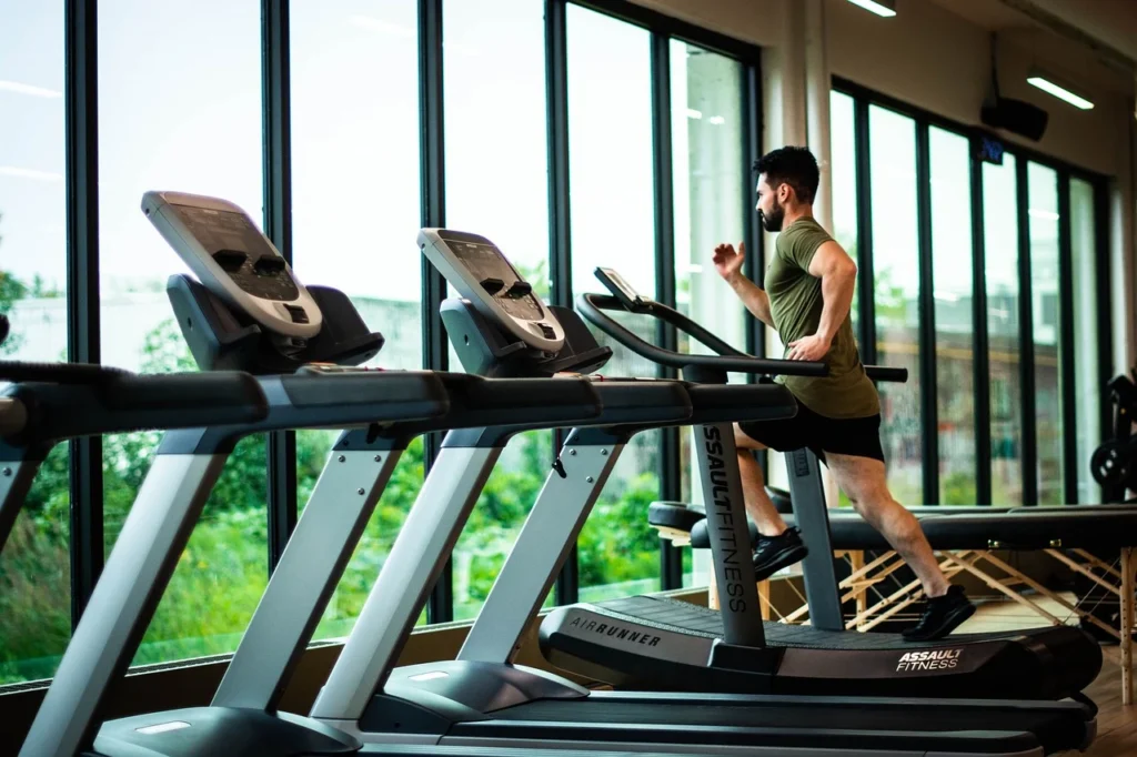 Man running on a treadmill in a gym, demonstrating cardio training for beginners. He is focused on his workout, surrounded by other treadmills and gym equipment. The setting highlights an energetic and supportive fitness environment for cardiovascular exercises.